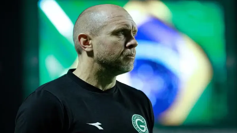 Técnico Mozart Santos em campo durante partida de futebol, com fundo de torcida em estádio, em Goiânia, Goiás.